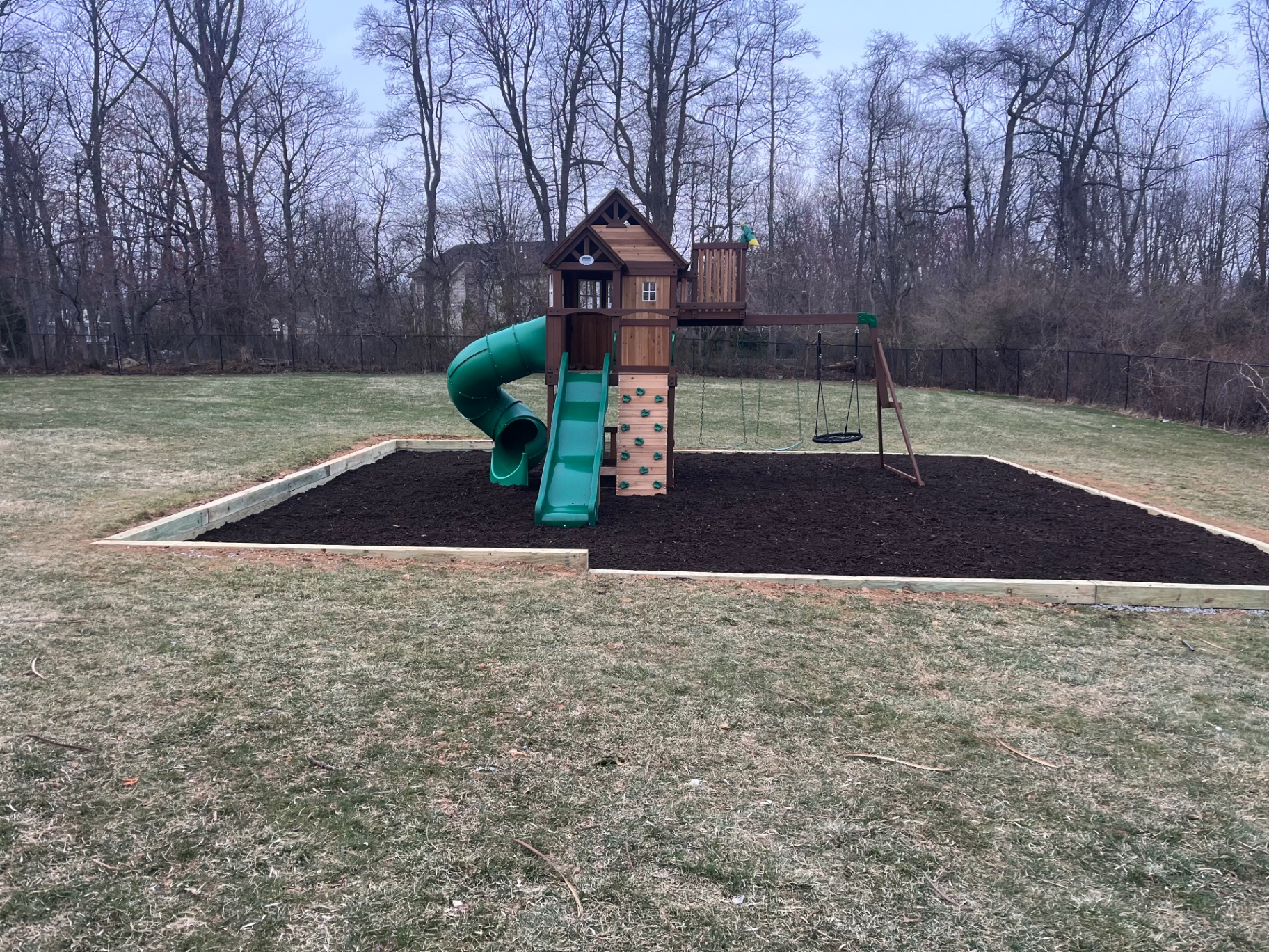 After photo of a finished backyard playground area with mulch base and playset.